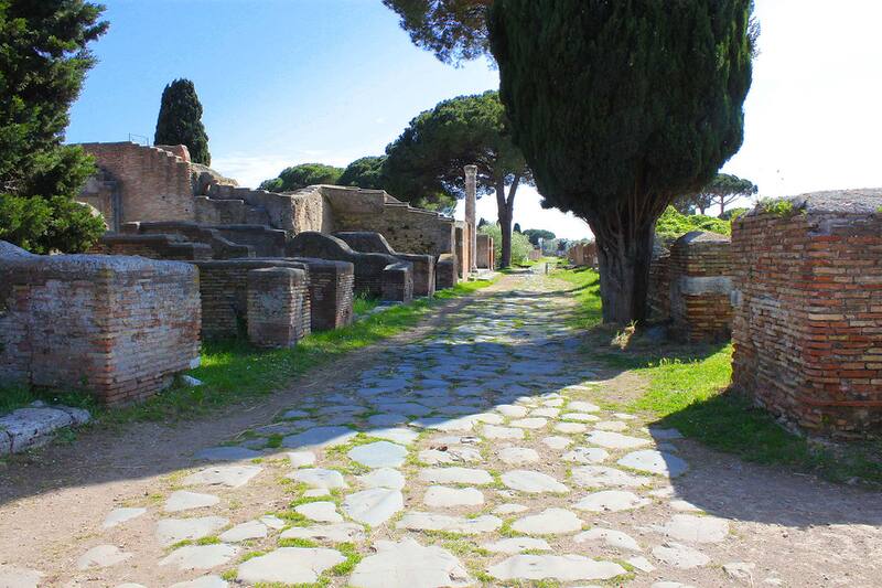 Decumanus Maximus, stone-paved road flanked by ruins and pines